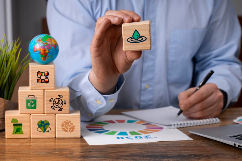 A person holds a wooden block with a water droplet icon. Other blocks with environmental symbols and a small globe are on the table. Sustainable theme.