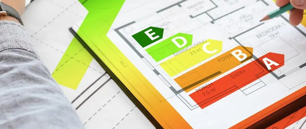 Blueprint design with energy efficiency ratings overlaid: E in green to A in red. A hand holds a pencil, indicating thoughtful planning.